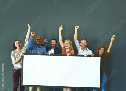 Excited business people showing a blank sign, promoting a product and giving a message on a board while standing together in an office at work. Portrait of happy colleagues holding an empty poster