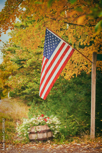 American flag hanging on the roadside against golden autumn foliage and beautiful pot flowers.