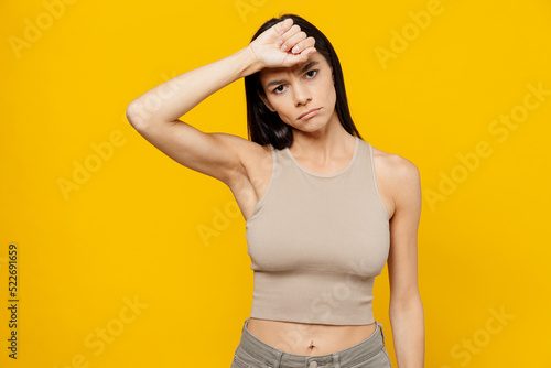 Young sad sick tired exhausted latin woman 30s she wear basic beige tank shirt put hand on forehead suffer from headache isolated on plain yellow backround studio portrait People lifestyle concept.