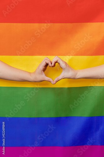 Cropped two adult young lesbian women show heart-shape sign with hands isolated on colorful rainbow symbol striped flag background studio People lgbtq lifestyle homosexual love relationship concept