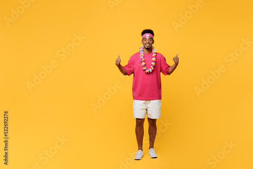 Full body young smiling happy fun man 20s he wear pink t-shirt hawaiian lei bandana near hotel pool showing thumb up like gesture isolated on plain yellow background. Summer vacation sea rest concept.