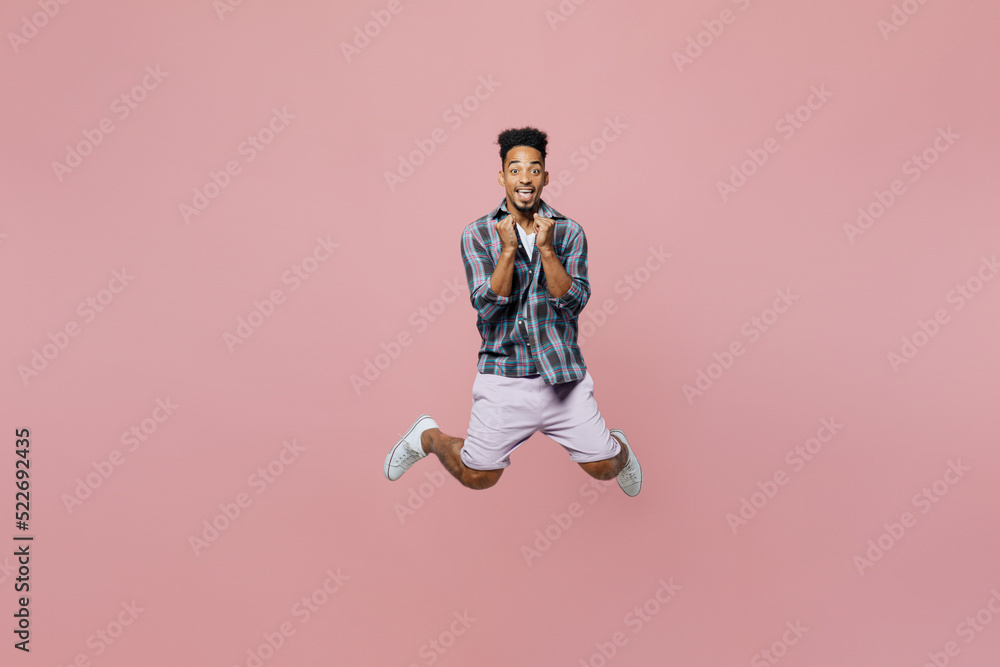 Full size young happy man of African American ethnicity 20s he wear blue shirt look camera jump high do winner gesture isolated on plain pastel light pink background studio. People lifestyle concept.