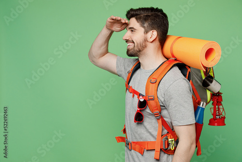 Young happy traveler white man carry backpack stuff mat look far away distance isolated on plain green background Tourist lead active lifestyle walk on spare time Hiking trek rest travel trip concept