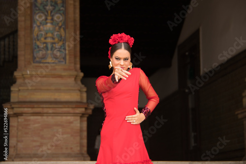Portrait of young teenage woman in red dance suit with ruffles and red carnations in her hair doing flamenco poses. Flamenco concept, dance, art, typical Spanish dance.