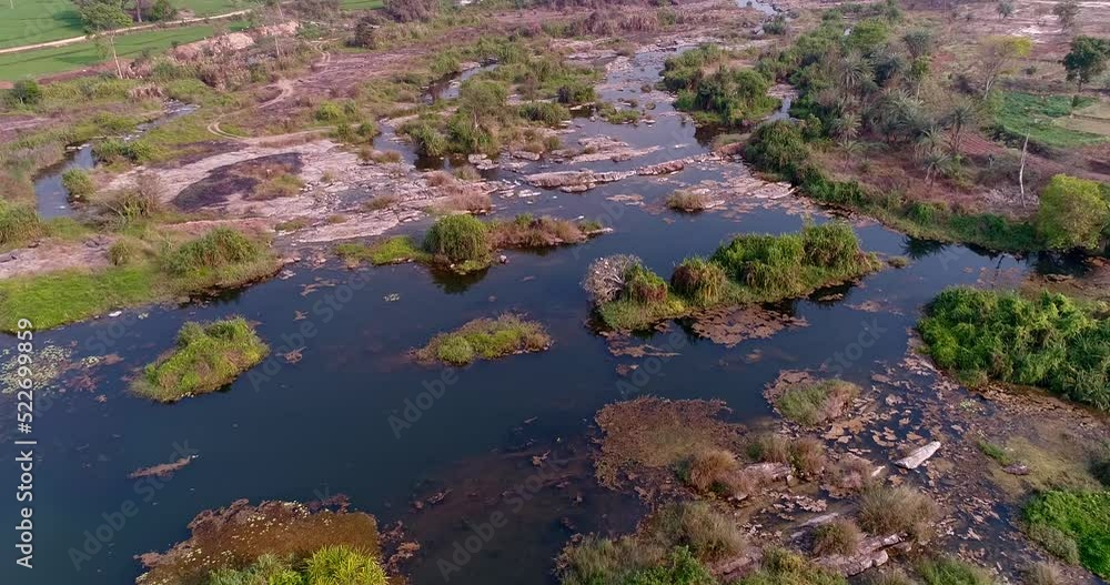 Aerial shot of rocky river bed, red soil and bright green rice fields along it Aerial shot of rocky river bed, red soil and bright green rice fields along it