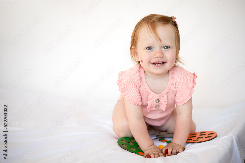 A wonderful cute little baby girl with red hair plays and laughs. Birthmark. Hemangioma. White background, space for text. Lifestyle. A wonderful cute little baby girl with red hair plays and laughs. Birthmark. Hemangioma. White background, space for text. Lifestyle.