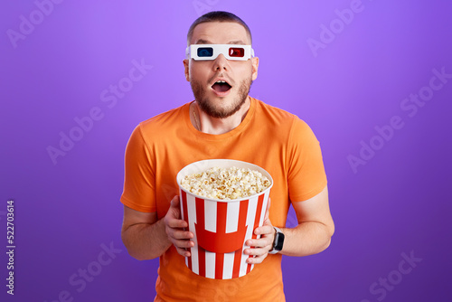 Young caucasian man in 3d glasses eating popcorn
