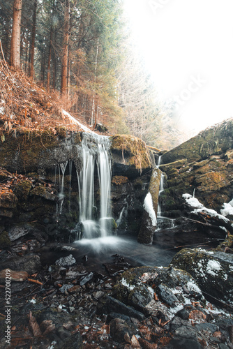 Clear water photographed with long exposure time through flowing rocks covered with moss with autumn colours of leaves and snow cover around. Beskydy mountains, czech republic, heart of Europe photo