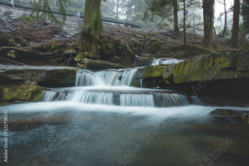 Clear water photographed with long exposure time through flowing rocks covered with moss with autumn colours of leaves and snow cover around. Krasna, Beskydy mountains, czech republic, heart of Europe © Fauren