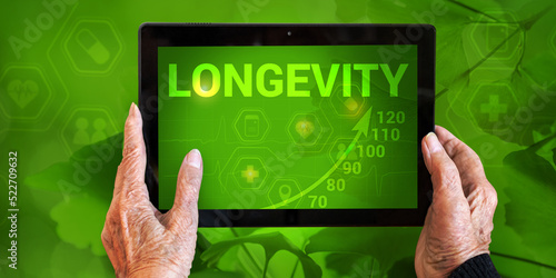 Fotografie Tablet with inscription Longevity and graph of increasing age in hands of elderly woman