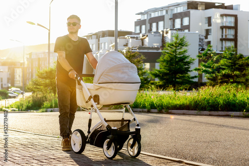 a young father walks with a stroller down the street. Walk with the child in the fresh air. photo