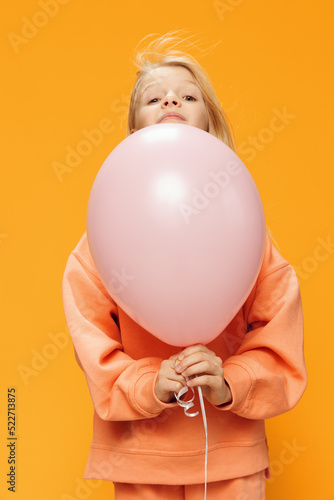 funny, happy girl stands peeking out from behind a pink balloon on an orange background in orange clothes © Tatiana