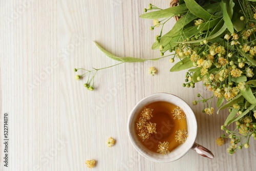 Cup of aromatic tea with linden blossoms on white wooden table, flat lay. Space for text