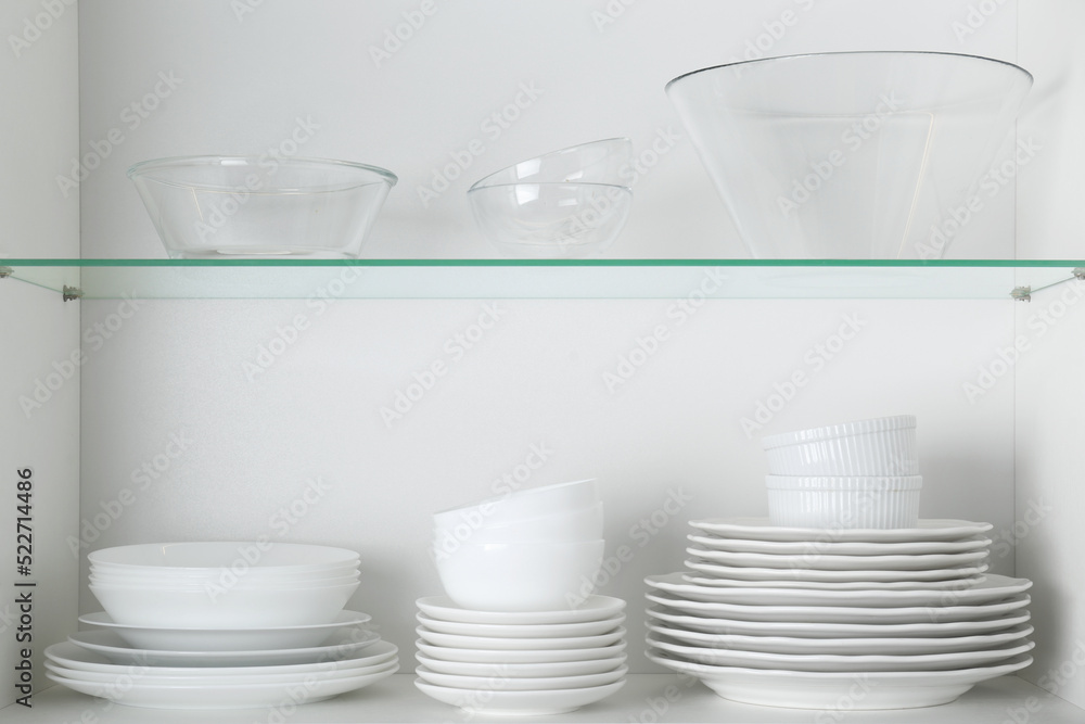 Different clean plates and bowls on shelves in cabinet - obrazy, fototapety, plakaty 