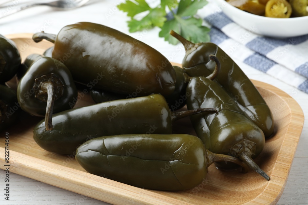 Wooden tray with pickled green jalapeno peppers on white table, closeup