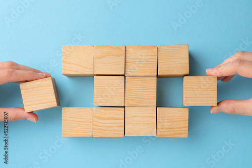 People holding wooden cubes near others on light blue background, top view. Management concept