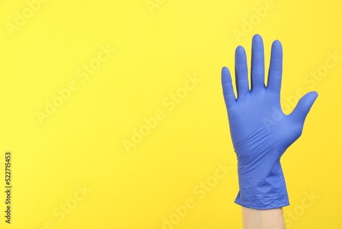 Person in medical gloves on yellow background, closeup of hand. Space for text
