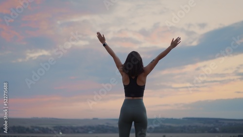 Back view of the beautiful woman wearing sports clothing relaxing and deeply breathing on the hill on the grass