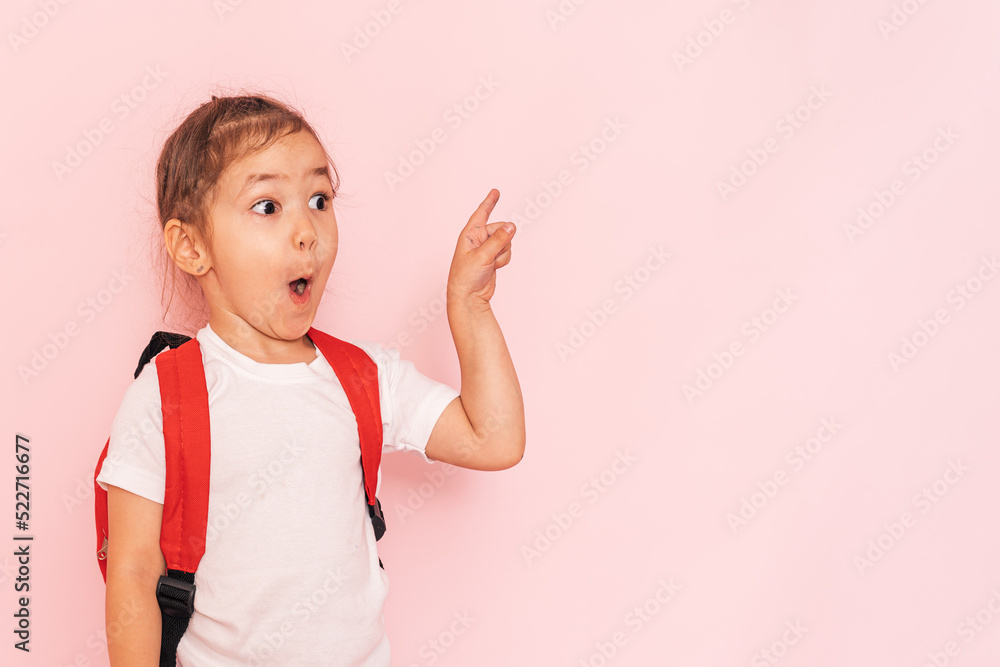 Surprised little girl with a red briefcase points her finger against a pink background. Surprised little girl with a red briefcase points her finger against a pink background.