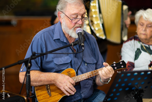senior gentleman singing and playing a ukulele with lady looking on photo
