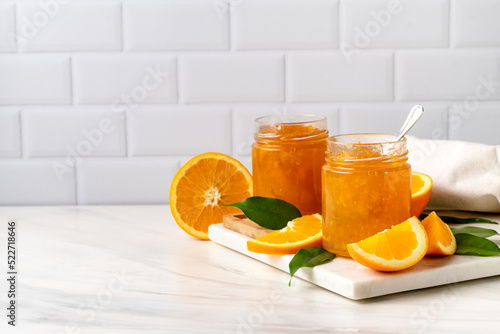 Orange jam in a glass jar and fresh oranges on a white marble background photo