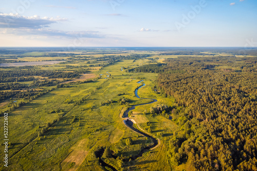 Beautiful aerial landscape of small river in countryside in evening. River near wild pine forest, warm sun rays illuminating valley