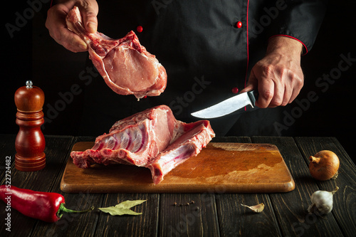Cook cuts raw ribs on a cutting board before baking. Cooking delicious food in the kitchen