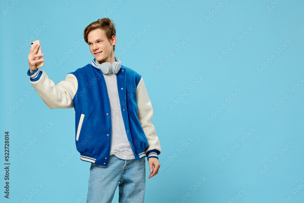 handsome stylish young man takes a selfie on the phone with his arm outstretched while standing with headphones around his neck handsome stylish young man takes a selfie on the phone with his arm outstretched while standing with headphones around his neck