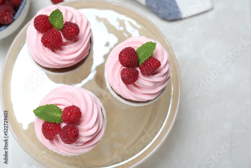 Delicious cupcakes with cream and raspberries on light grey marble table, flat lay