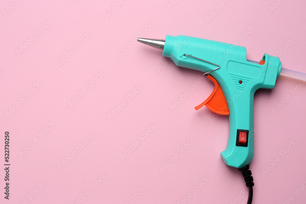 Turquoise glue gun with stick on pink background, top view. Space for text Turquoise glue gun with stick on pink background, top view. Space for text