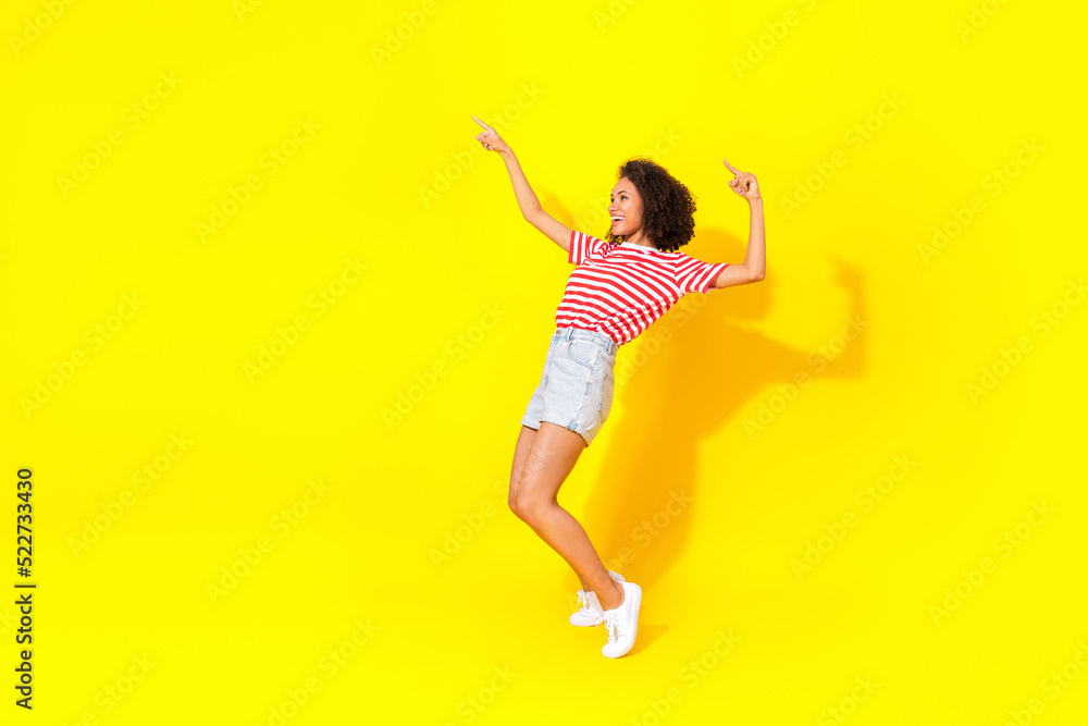 Full length photo of young smiling dancing lady stay toes directing empty space new sale isolated on yellow color background Full length photo of young smiling dancing lady stay toes directing empty space new sale isolated on yellow color background
