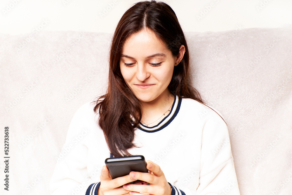 Young woman at home using Smartphone, scrolling through social networks. She is sitting on a sofa Young woman at home using Smartphone, scrolling through social networks. She is sitting on a sofa