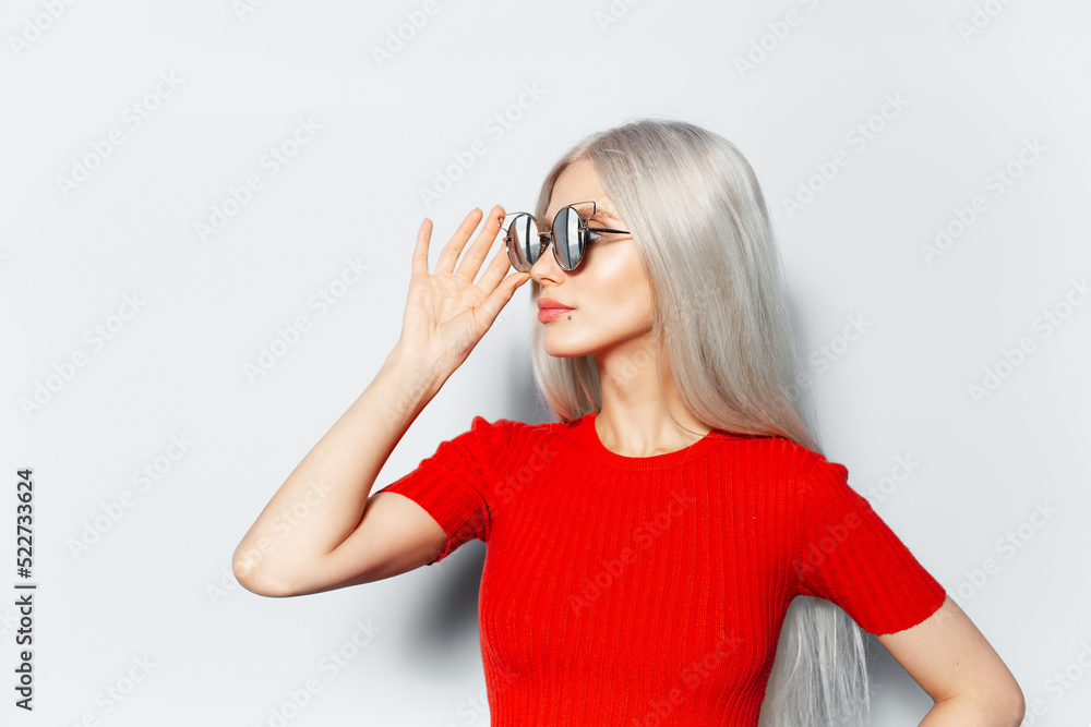 Studio side portrait of young blonde pretty girl wearing sunglasses and red shirt, looking away on white background. Studio side portrait of young blonde pretty girl wearing sunglasses and red shirt, looking away on white background.