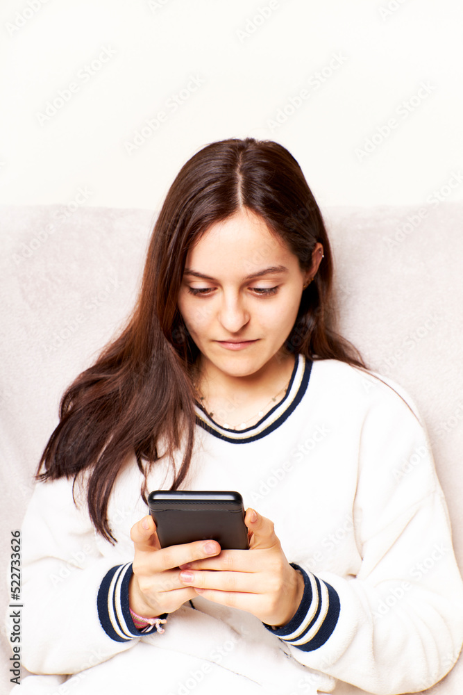 Young woman at home using Smartphone, scrolling through social networks. She is sitting on a sofa Young woman at home using Smartphone, scrolling through social networks. She is sitting on a sofa