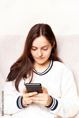 Young woman at home using Smartphone, scrolling through social networks. She is sitting on a sofa
