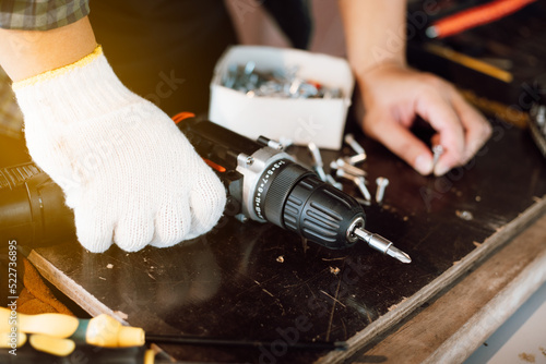 Close up of male mechanic holding electric cordless screwdriver drill with wood screw in the factory. Working with the screw. Professional carpenter. Concept furniture at home.