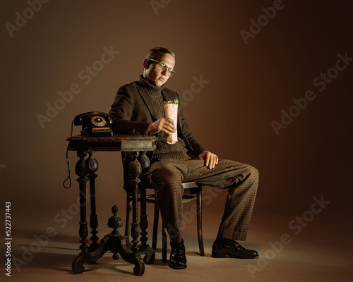 Retro style portrait of young man, writer and traveler wearing vintage style clothes isolated over dark brown background. Business, art, fashion concept