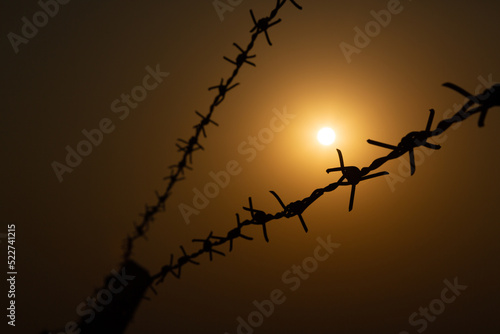 Selective focus of barbed wire silhouette on sunset background.