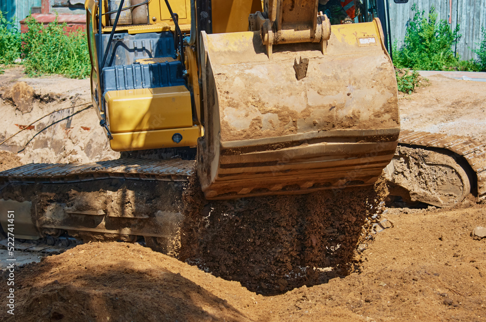 Fototapeta premium Close up view of an excavator bucket full of earth. The process of digging soil at a construction site. Selective focus