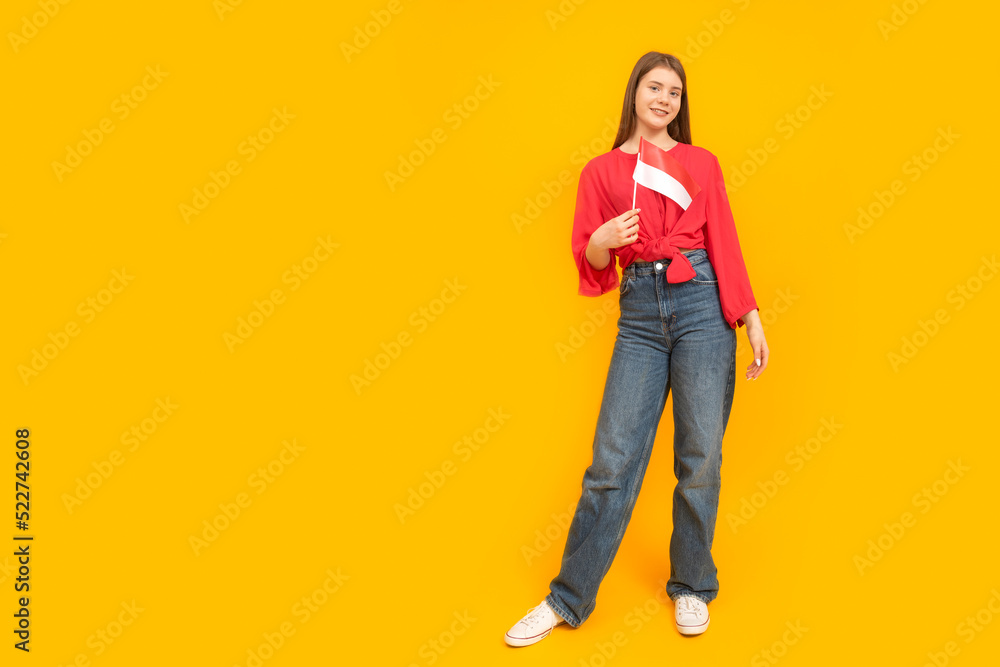 Full-length portrait of young girl on yellow background. Teenager holds the flag of Monaco or Indonesia. Full-length portrait of young girl on yellow background. Teenager holds the flag of Monaco or Indonesia.