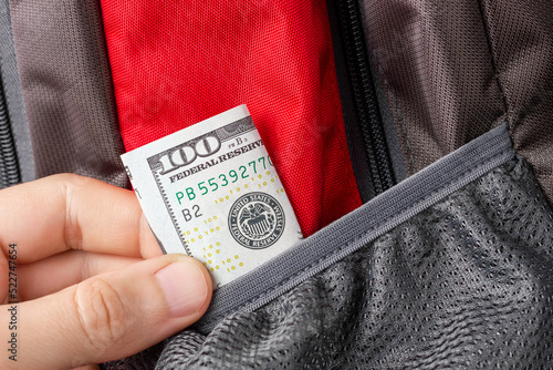 A thief's hand pulls a hundred dollar bill out of a backpack pocket. Pickpocket activities.