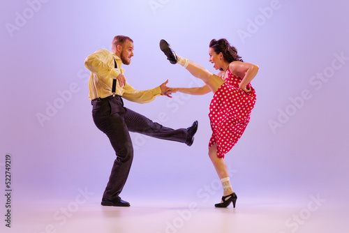Beautiful girl and man in colorful retro style costumes dancing incendiary dances isolated on lilac color background in neon light. Concept of art, culture