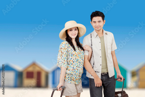 Happy young couple carrying luggage on beach