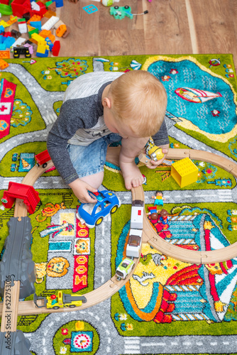 Adorable little boy playing with colorful plastic construction blocks at home, sitting on the floor, train going on railroad. Creative games for kids photo