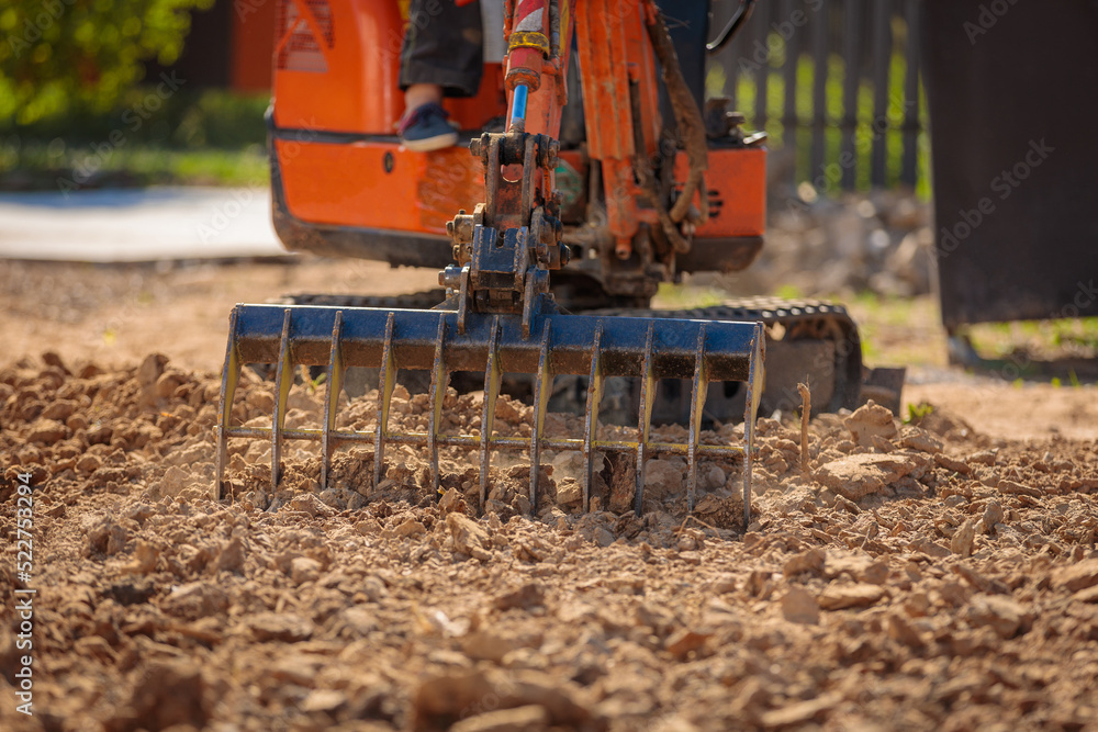 Obraz premium A mini excavator with a rake loosens the ground. landscape preparation