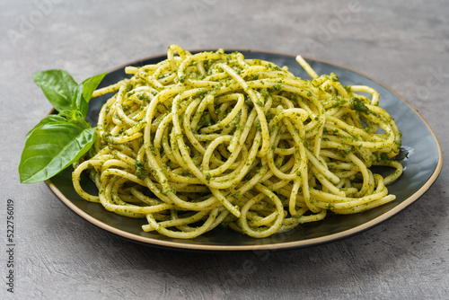 Plate of spaghetti with pesto sauce on gray stone background.