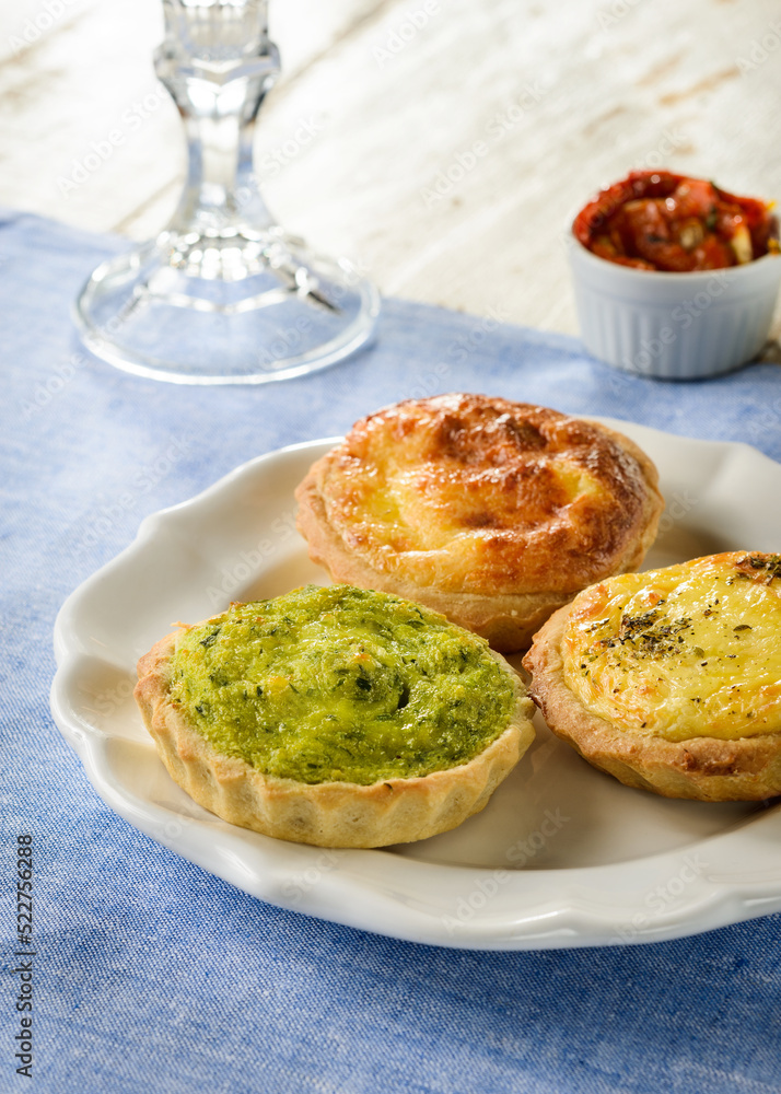 Three delicious quiches of different flavors on a ceramic plate, on a blue placemat, with wood table set Three delicious quiches of different flavors on a ceramic plate, on a blue placemat, with wood table set