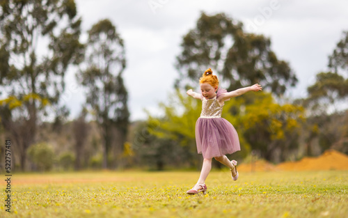 little red-headed girl leaping outdoors wearing pretty sequinned dress