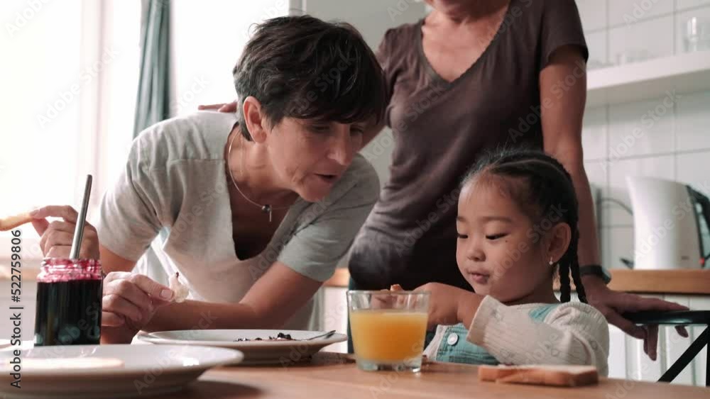 Lovely mature lesbian couple eating breakfast with adopted Asian daughter in the kitchen at home Lovely mature lesbian couple eating breakfast with adopted Asian daughter in the kitchen at home