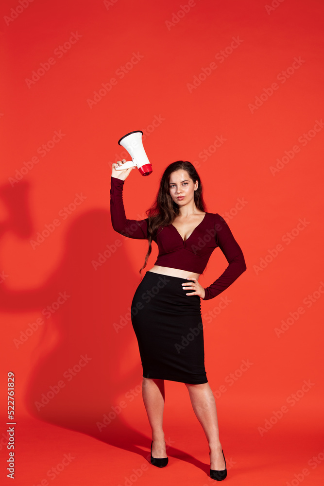 Portrait of stylish young woman posing with megaphone isolated over red studio background. Expressive news, big sales Portrait of stylish young woman posing with megaphone isolated over red studio background. Expressive news, big sales
